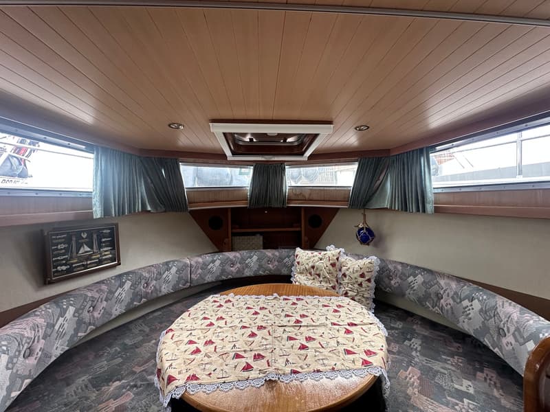 De foto toont een interieur van een boot met een ronde tafel, een U-vormige bank en ramen met gordijnen. — Boarncruiser 1000