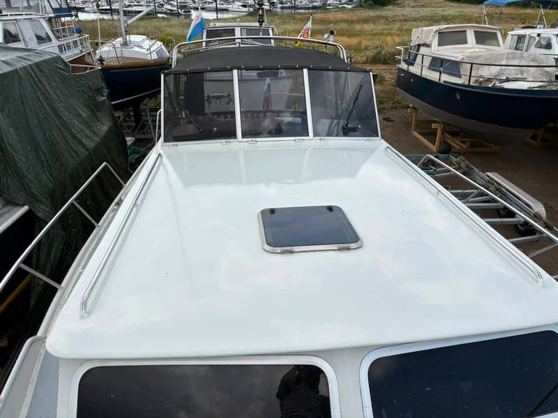 Een witte boot met een zwart dak en een luik op het voordek, omringd door andere boten op het land. — Valk Sport