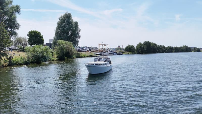 Een witte motorboot vaart op een waterweg met bomen langs de oevers en een jachthaven in de verte. — Valk Sport