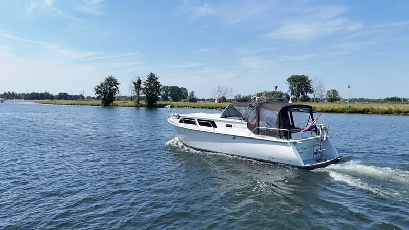 Een witte motorboot met een zwarte kap vaart op een waterweg met land aan de horizon. — Valk Sport