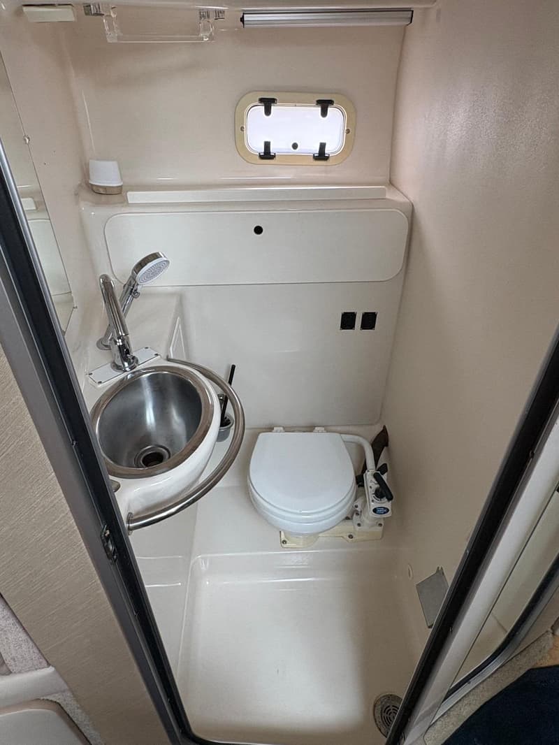 De foto toont een compacte badkamer in een boot met een toilet, wastafel met douchekop en een klein raam. — Maxum 3200 SCR