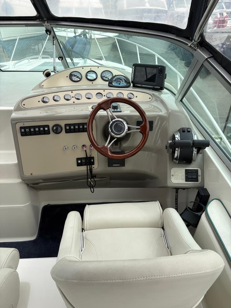 De foto toont het stuur en het dashboard van een boot met diverse meters, schakelaars en een Lowrance navigatiesysteem.
