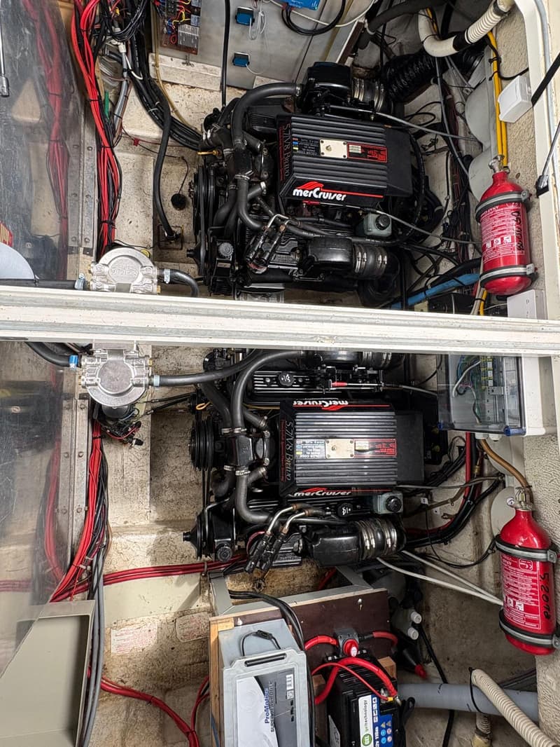 Twee zwarte MerCruiser 5.7 V8 Bravo motoren zijn zichtbaar, met rode brandblussers en accu's eromheen.