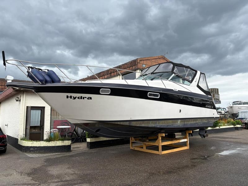 Een witte boot met zwarte accenten en de naam "Hydra" op de boeg, staat op een houten bok. — Maxum 3200 SCR