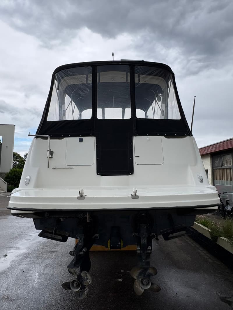 Een witte motorboot met een zwarte kap en doorzichtige ramen staat op het droge, met twee schroeven zichtbaar aan de…