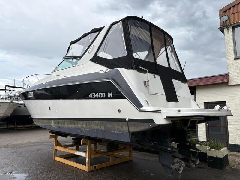 Een witte motorboot met zwarte accenten en een zwarte cabrioletkap staat op een houten bok op een natte ondergrond.