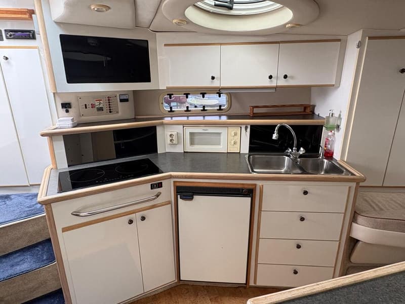 Een interieur van een boot met een keukenblok, inclusief kookplaat, spoelbak, magnetron en koelkast. — Maxum 3200 SCR