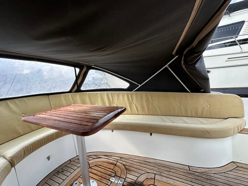 Een houten tafel met een metalen poot staat op een houten vloer, omringd door beige kussens en een donker zeil.