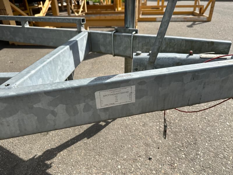 Een close-up van een gegalvaniseerd metalen frame met een wit label met zwarte tekst en een rode draad.