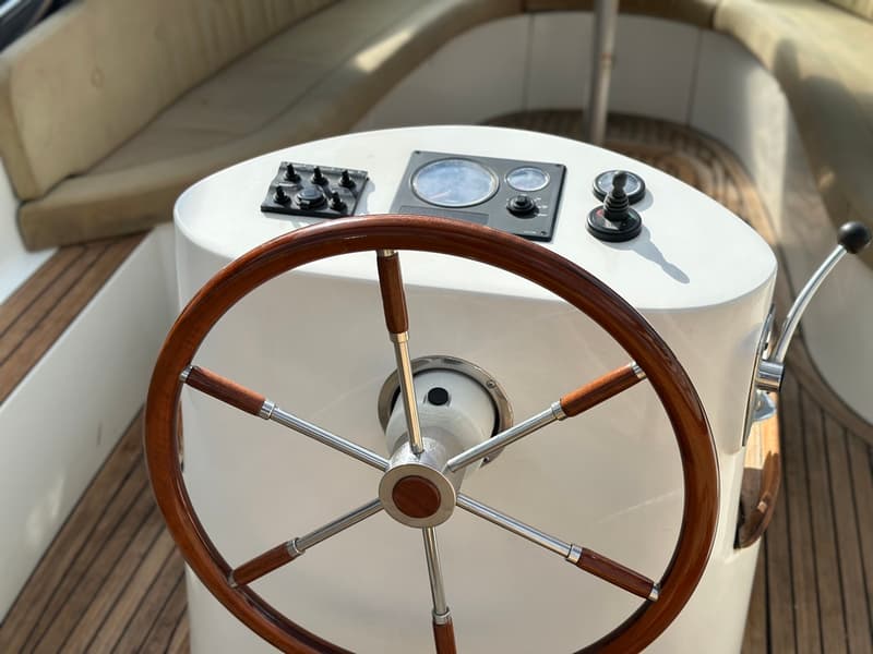 Een houten stuurwiel met metalen spaken en een wit dashboard met meters en schakelaars.