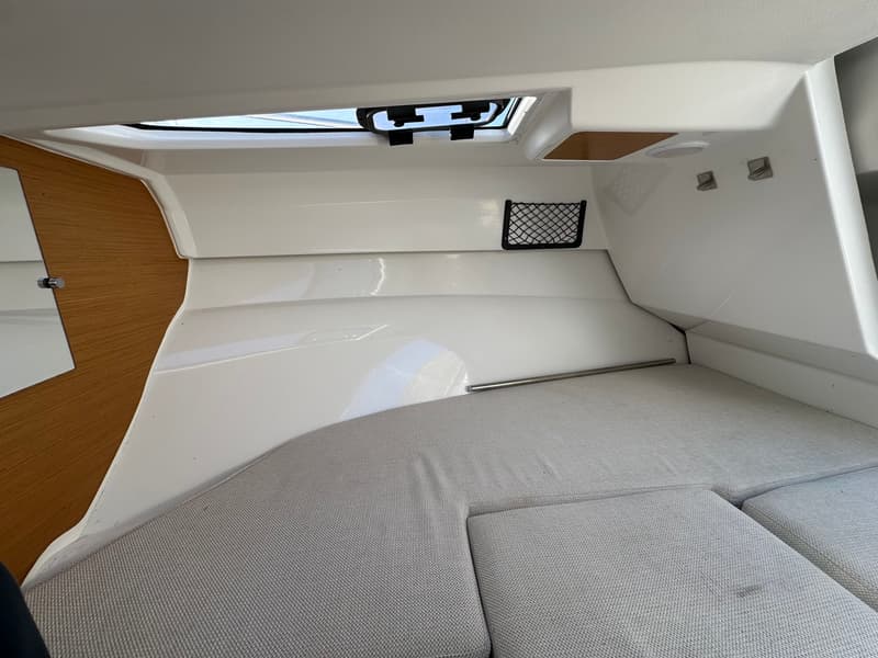 De foto toont een kajuit met een wit interieur, grijze kussens, een houten wand en een dakluik. — Jeanneau Cap Camarat