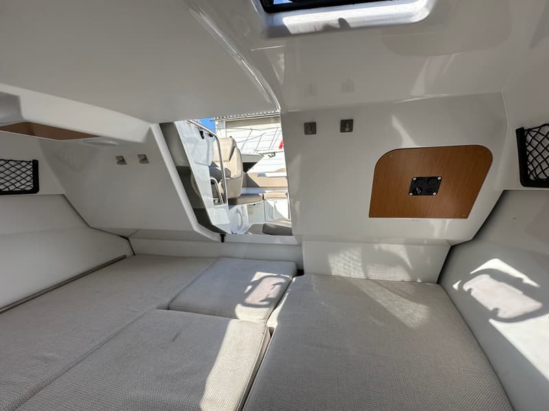 De foto toont het interieur van een bootkajuit met lichte kussens en een houten paneel met schakelaars.