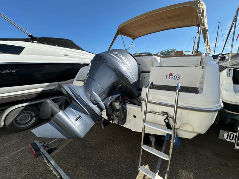 Een witte boot met een grijze Yamaha buitenboordmotor staat op een trailer, met een beige biminitop en een zwemtrap.