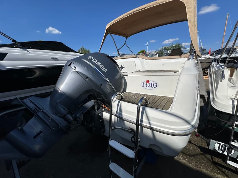 Een witte boot met een Yamaha buitenboordmotor, een beige biminitop en een zwemtrap aan de achterzijde.