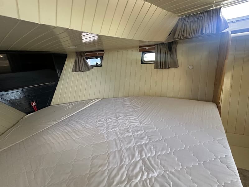 Een kajuit met een groot wit matras, twee kleine ramen met gordijnen en een wit houten plafond en wanden. — Oomen kruiser fly