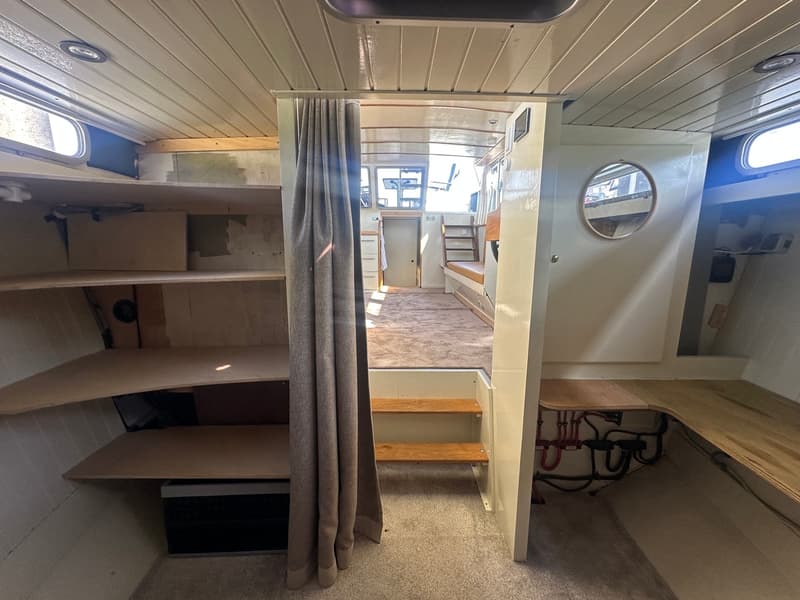 De foto toont het interieur van een boot met een doorkijk naar een andere ruimte, met planken, een gordijn en een…
