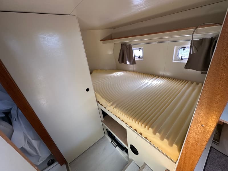 De foto toont een kajuit met een bed met een geribbeld matras, twee patrijspoorten en een witte kastdeur. — Oomen kruiser fly