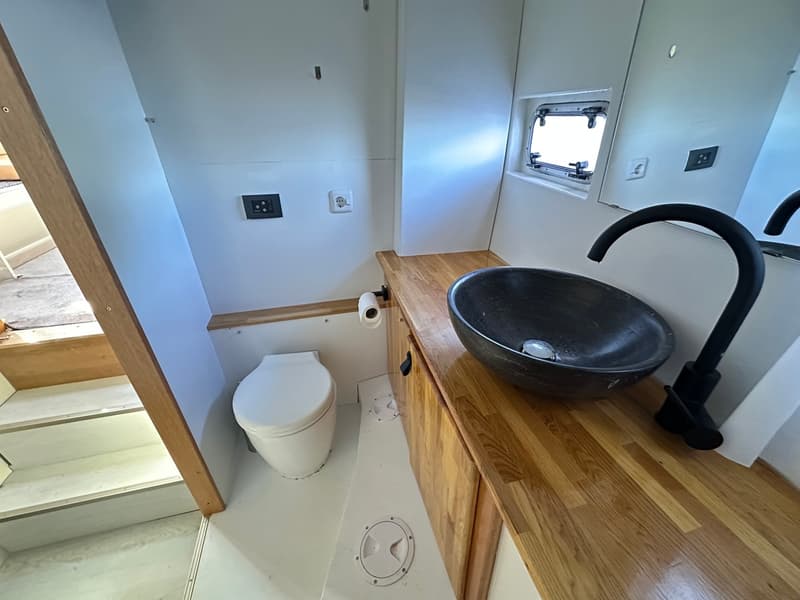 Een badkamer met een wit toilet, een donkere wasbak met zwarte kraan, een houten aanrecht en een spiegel.
