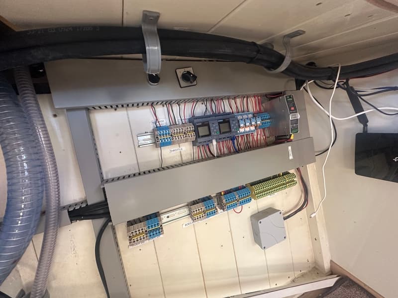 Een elektrisch paneel met diverse bedrading, schakelaars en modules is zichtbaar, met slangen en kabels ernaast.