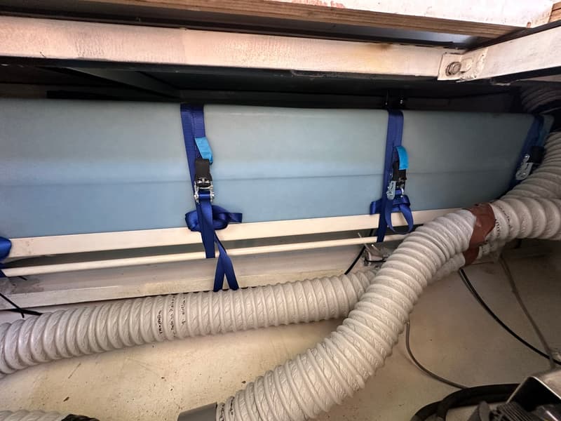 Een lichtblauwe tank is vastgezet met blauwe spanbanden boven twee witte flexibele slangen.