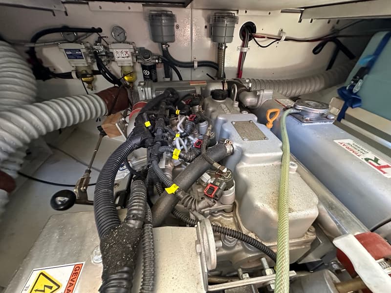 Een detailfoto van een scheepsmotor met diverse slangen, kabels en filters in een motorruimte.
