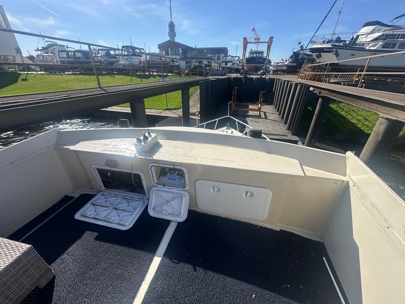 De foto toont de achtersteven van een boot met een donkere vloerbedekking, twee open luiken en een bedieningspaneel.