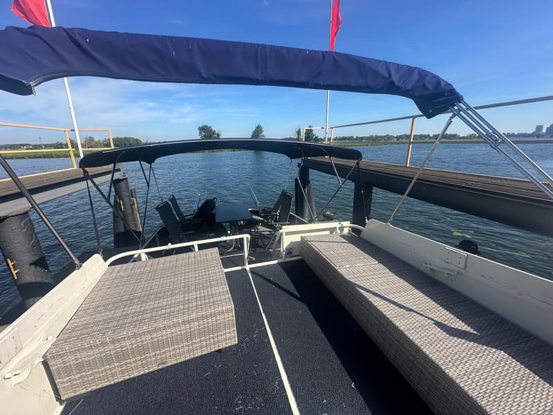 De achterkant van een boot met een donkerblauwe biminitop, twee rieten banken en een tafel met stoelen. — Oomen kruiser fly