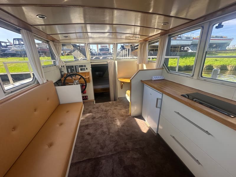 De foto toont het interieur van een boot met een stuurstand, bank, keukenblok en uitzicht naar buiten. — Oomen kruiser fly
