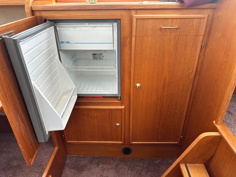 Een open koelkast is ingebouwd in een houten meubel met een kast en lade.