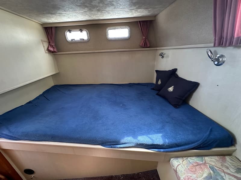 Een kajuit met een tweepersoonsbed met blauw beddengoed en twee kussens met zeilbootmotief. — Succes Ultra 500