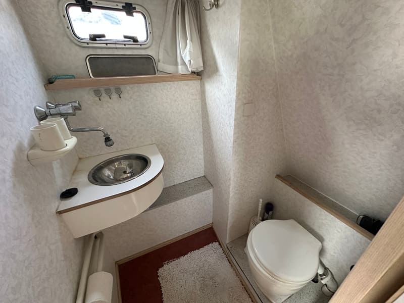 Een kleine badkamer met een toilet, een wastafel met kraan, een raam en een spiegel.