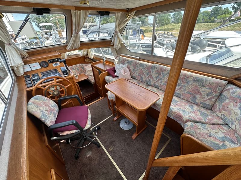 Een interieur van een boot met een stuurwiel, een draaibare stoel, een bank en een tafel. — Succes Ultra 500