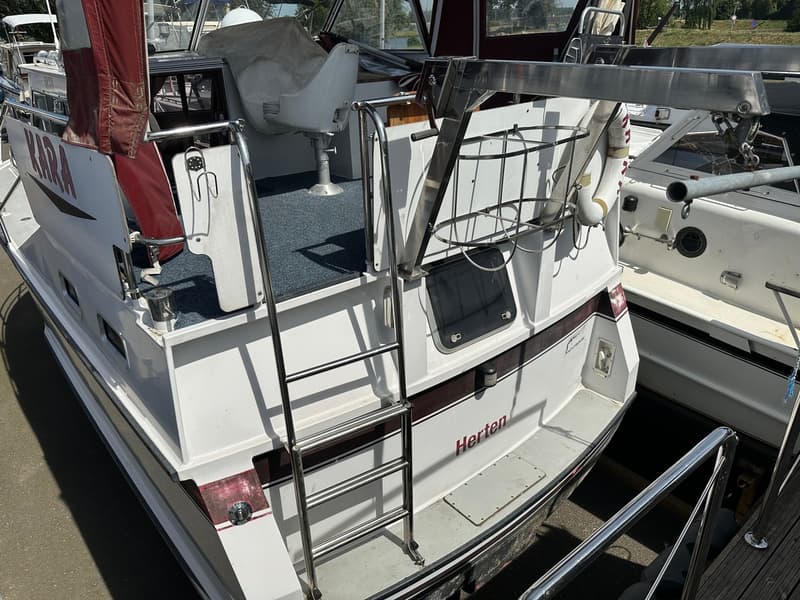 Een witte boot met een roodbruine streep en de naam "Herten" op de achtersteven, met een zwemtrap en een davit.