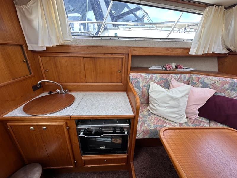 Een interieur van een boot met een keukenblok, een bank met kussens en een houten tafel. — Succes Ultra 500