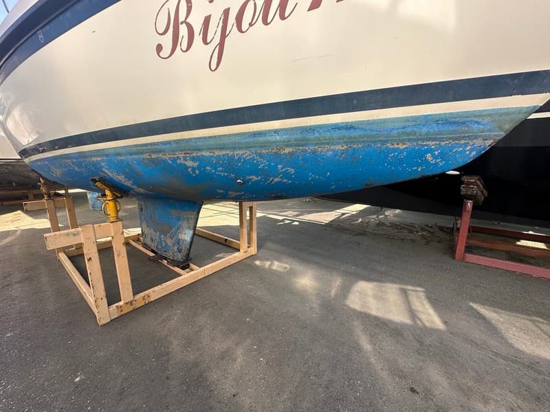 De foto toont de romp van een boot met een blauwe onderkant en een witte bovenkant, staand op een houten bok. — Compromis 777