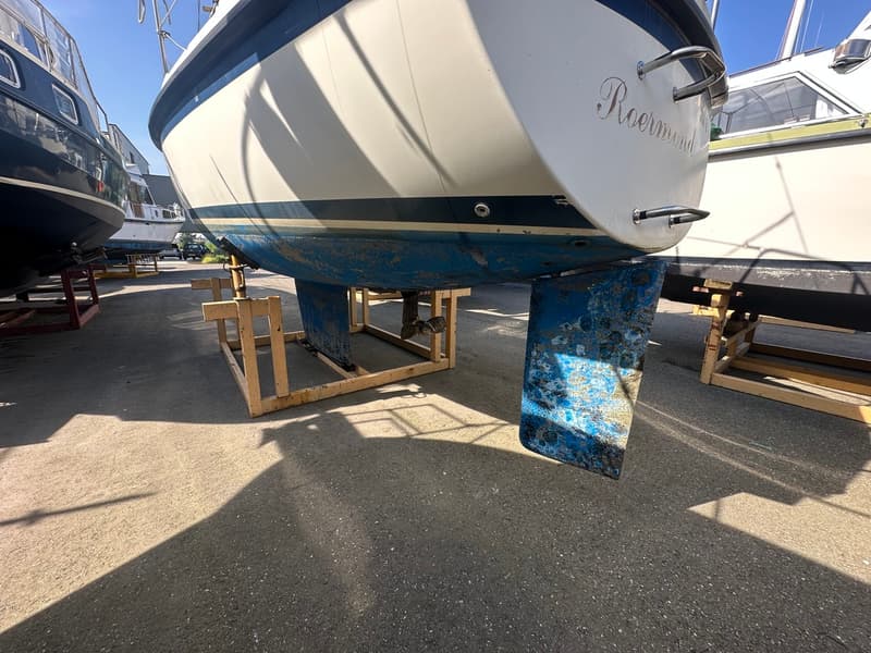 Een witte boot met blauwe onderkant en roer staat op houten bokken op een geasfalteerd terrein. — Compromis 777
