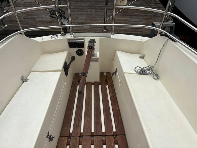 De foto toont het interieur van een boot met een zithoek, een kombuis met spoelbak en kookplaat, en houten kasten.