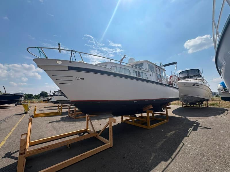 Een witte boot met de naam "Nino" op de boeg staat op een trailer op een buitenterrein onder een blauwe lucht.