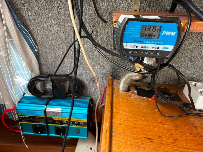 Een blauwe omvormer en een zonnelaadregelaar met een display van 13.8V zijn zichtbaar, met diverse kabels.