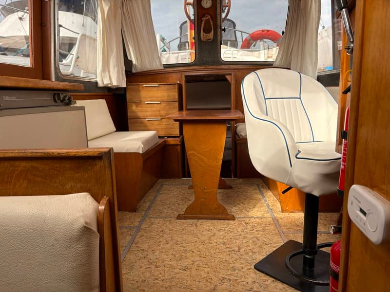 De foto toont het interieur van een boot met houten meubilair, een witte stoel en een tafel. — Smelne 950 ak