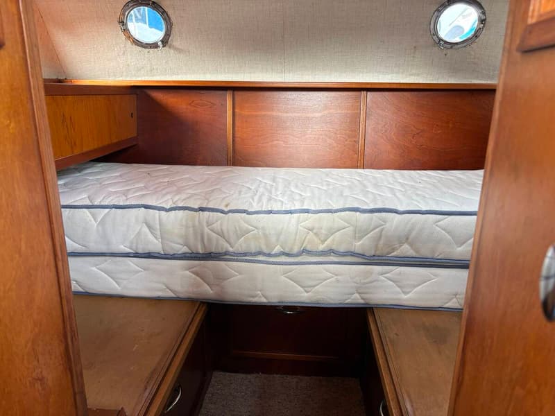 Een kajuit met een wit matras, houten wanden en twee patrijspoorten. — Smelne 950 ak