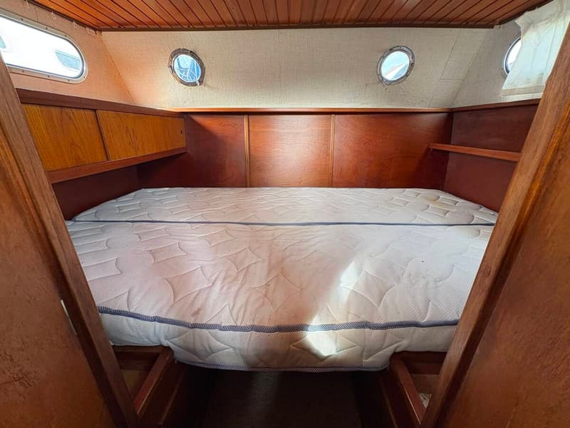 De foto toont een kajuit met een tweepersoonsbed, houten wanden en plafond, en twee patrijspoorten. — Smelne 950 ak