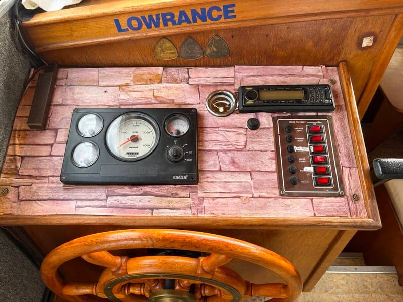 Een houten stuurwiel en een dashboard met meters, schakelaars en een radio zijn zichtbaar.