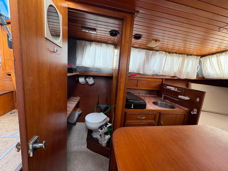 De foto toont een interieur van een boot met een toiletruimte en een kombuis met gootsteen en kookplaat. — Smelne 950 ak