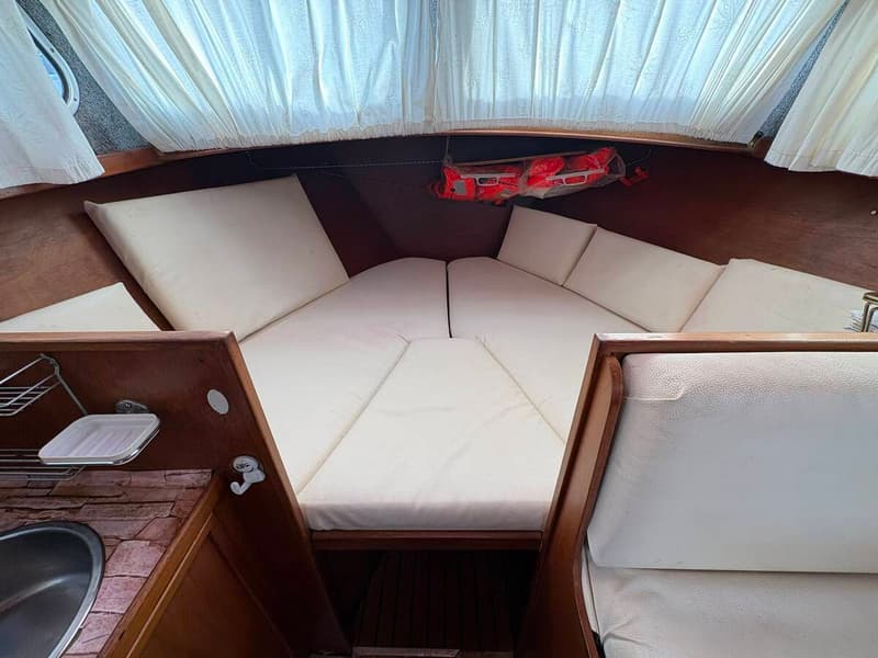 De foto toont het interieur van een boot met een V-vormige slaapplaats, witte kussens en gordijnen. — Smelne 950 ak