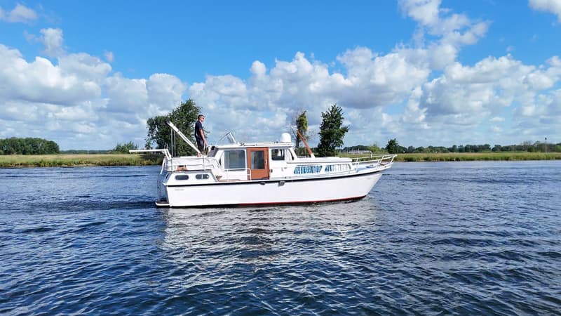 Een witte motorboot met een rode streep op de romp vaart op blauw water onder een bewolkte hemel. — Smelne 950 ak