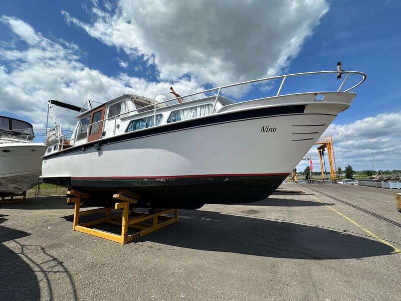 Een witte motorboot met de naam "Nino" op de boeg staat op een gele bok op een betonnen ondergrond onder een bewolkte hemel.