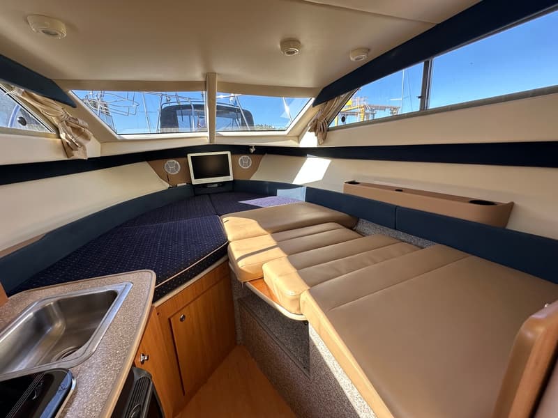 Twee boten liggen aangemeerd, de voorste boot is wit met een blauwe streep en heeft een anker aan de boeg.
