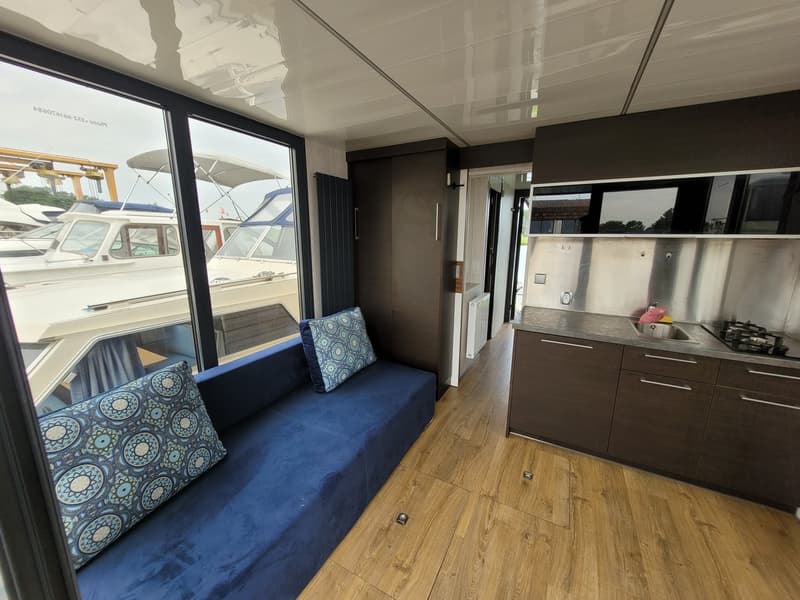 Een interieur van een boot met een blauwe bank, een keukenblok en grote ramen die uitkijken op andere boten. — Campi 320 LR