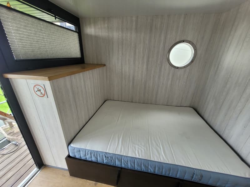 Een kajuit met een bed, een patrijspoort, een raam met plisségordijn en een houten plank. — Campi 320 LR